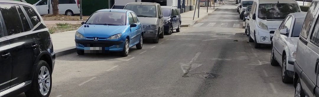 La calle del taller, con coches aparcados a los dos lados de la calzada.