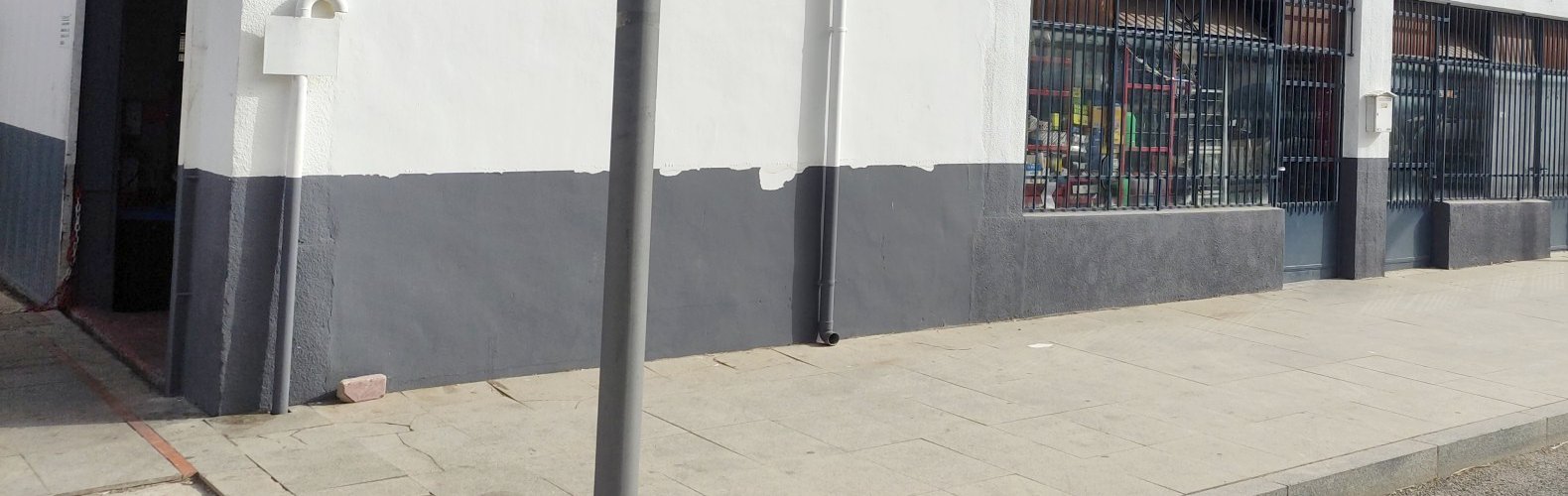 La fachada del taller a pie de avenida: el portón a la izquierda, acera ancha delante y los ventanales del taller a la derecha.