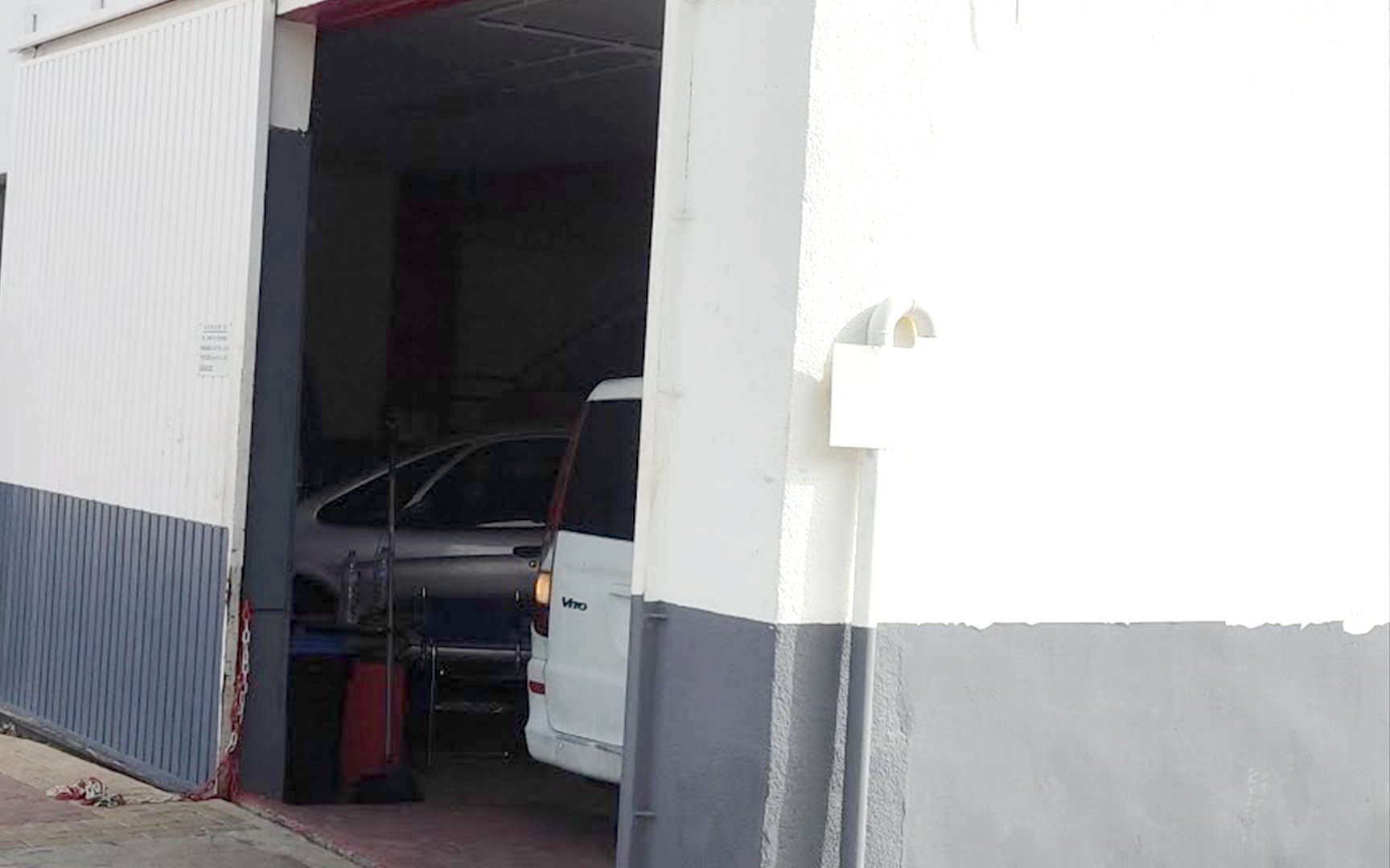 El portón corredero del taller, abierto de par en par sobre la avenida, con un turismo oscuro y una furgoneta blanca dentro de la nave.